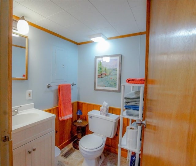 bathroom with toilet, wood walls, vanity, wainscoting, and crown molding