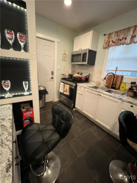 kitchen with light stone counters, backsplash, appliances with stainless steel finishes, white cabinets, and a sink