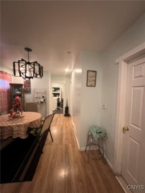 hallway featuring a chandelier, wood finished floors, and baseboards