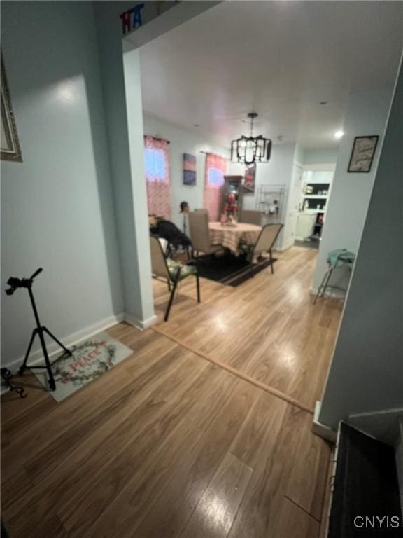 corridor featuring baseboards, an inviting chandelier, and wood finished floors