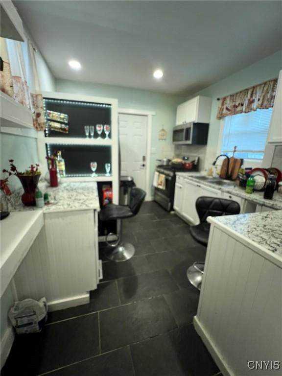 kitchen featuring white cabinets, stainless steel microwave, range, and a sink