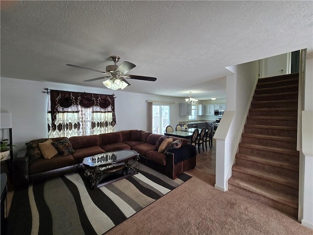 carpeted living area with ceiling fan with notable chandelier, stairway, and a textured ceiling