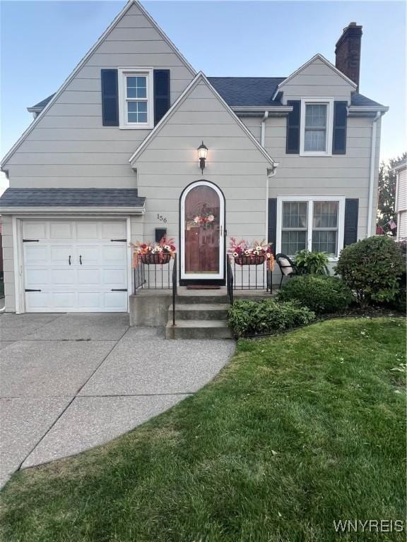 traditional home featuring an attached garage, concrete driveway, roof with shingles, a chimney, and a front yard