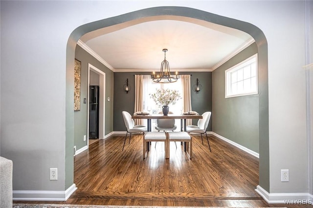 dining space featuring arched walkways, an inviting chandelier, ornamental molding, wood finished floors, and baseboards