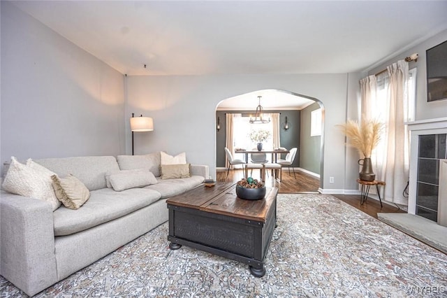 living area with arched walkways, a notable chandelier, wood finished floors, and baseboards