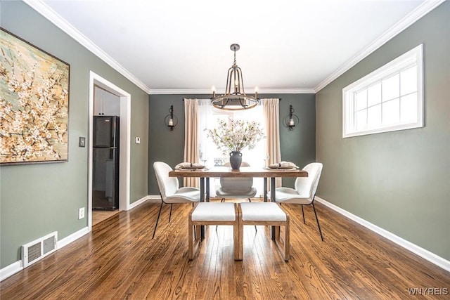 dining space featuring a notable chandelier, wood finished floors, visible vents, and crown molding