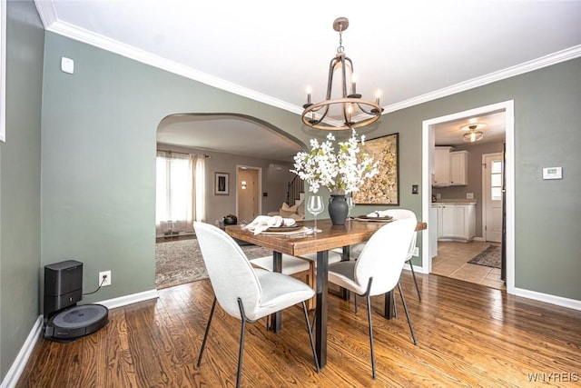 dining space featuring baseboards, arched walkways, wood finished floors, crown molding, and a notable chandelier