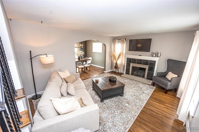 living room with baseboards, arched walkways, wood finished floors, and a tile fireplace