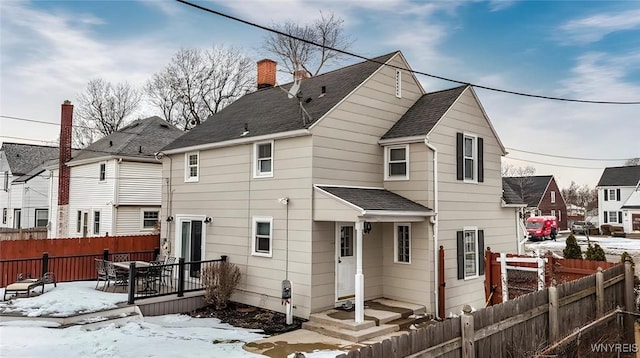 snow covered back of property featuring a shingled roof and fence private yard