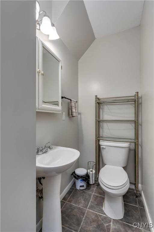 half bathroom with toilet, baseboards, lofted ceiling, and tile patterned floors