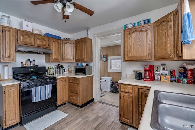 kitchen featuring stainless steel microwave, black range with gas stovetop, light countertops, under cabinet range hood, and a sink