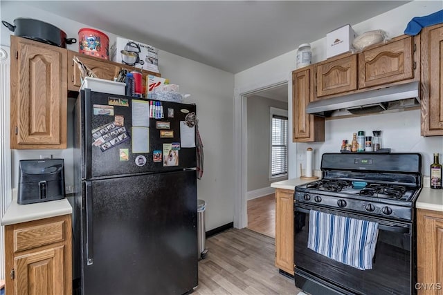 kitchen featuring light countertops, light wood-style flooring, black appliances, under cabinet range hood, and baseboards