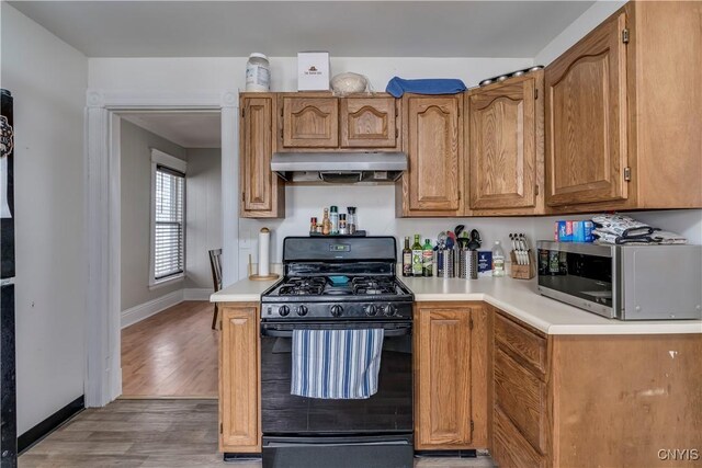 kitchen with black range with gas stovetop, extractor fan, stainless steel microwave, and light countertops