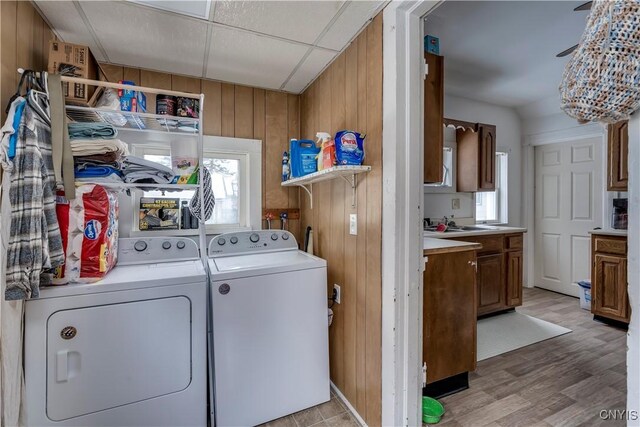 laundry area with washing machine and clothes dryer, light wood-style floors, a healthy amount of sunlight, wooden walls, and laundry area