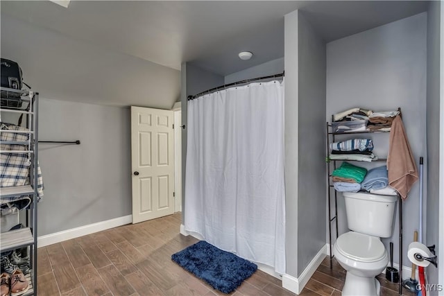 bathroom with lofted ceiling, curtained shower, toilet, wood finish floors, and baseboards