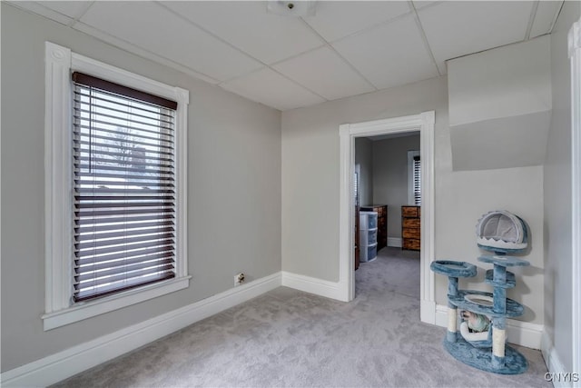 carpeted spare room featuring a drop ceiling and baseboards