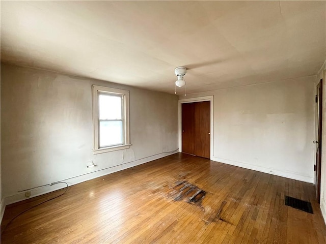 unfurnished room with ceiling fan, hardwood / wood-style floors, visible vents, and baseboards