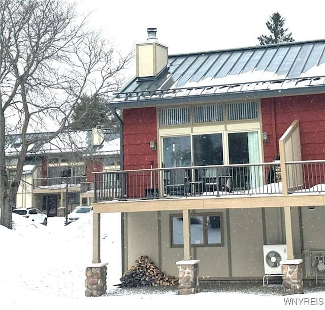 snow covered rear of property featuring a standing seam roof, metal roof, a chimney, and stucco siding