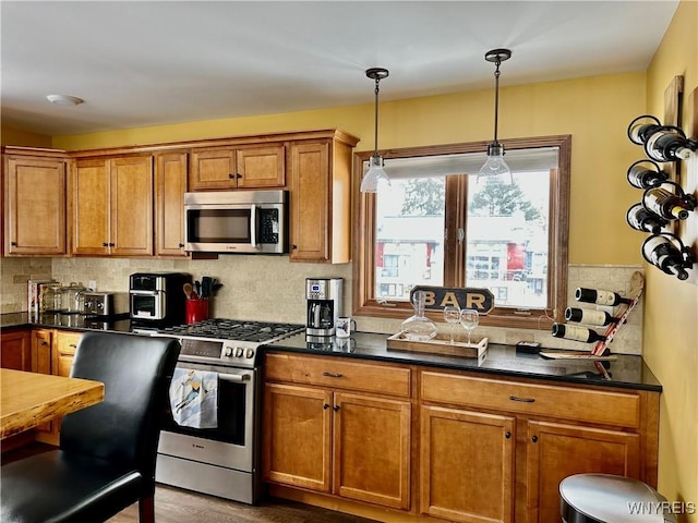 kitchen featuring appliances with stainless steel finishes, dark countertops, brown cabinetry, and hanging light fixtures