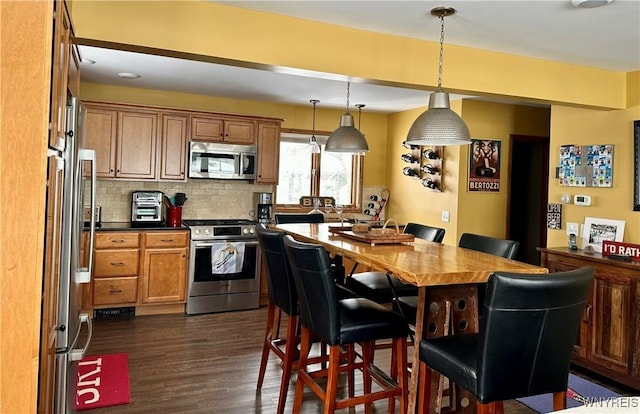 kitchen featuring stainless steel appliances, a breakfast bar, hanging light fixtures, backsplash, and dark wood finished floors