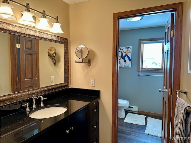 bathroom featuring toilet, a baseboard heating unit, vanity, wood finished floors, and baseboards