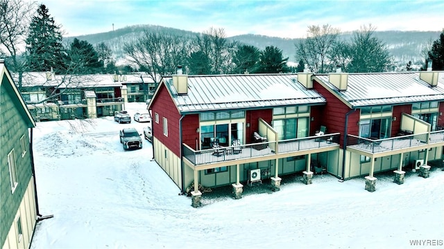 snow covered back of property with a standing seam roof, metal roof, and a chimney