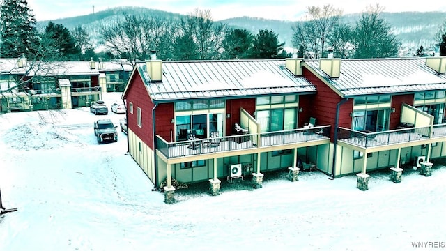 snow covered rear of property with a standing seam roof, metal roof, a chimney, and a mountain view