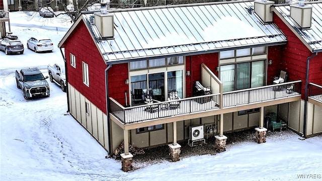 snow covered property featuring a standing seam roof, a chimney, metal roof, and ac unit