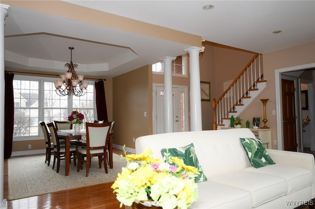 dining space featuring a chandelier, wood finished floors, stairway, a tray ceiling, and ornate columns