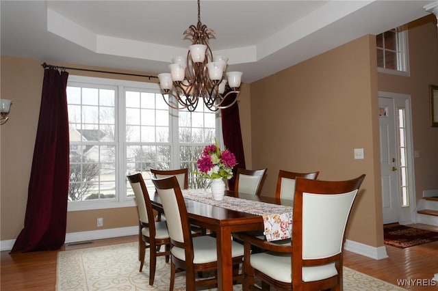 dining room with a chandelier, a tray ceiling, wood finished floors, and baseboards