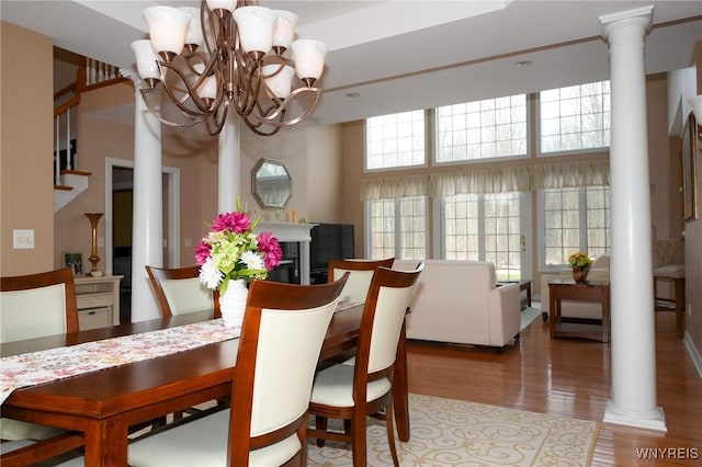 dining space with an inviting chandelier, a fireplace, ornate columns, and wood finished floors