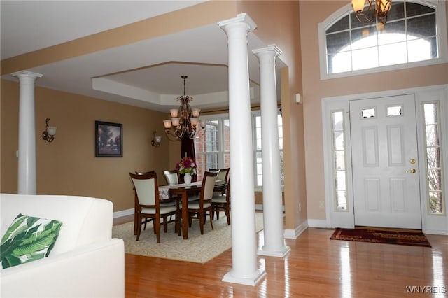 foyer featuring ornate columns, a tray ceiling, a wealth of natural light, and an inviting chandelier