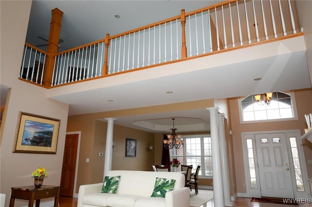 interior space featuring ornate columns, a tray ceiling, a high ceiling, and a notable chandelier