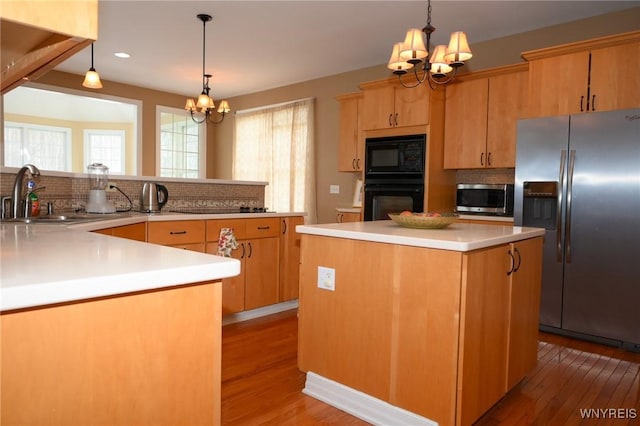 kitchen featuring light countertops, a sink, a kitchen island, a chandelier, and black appliances