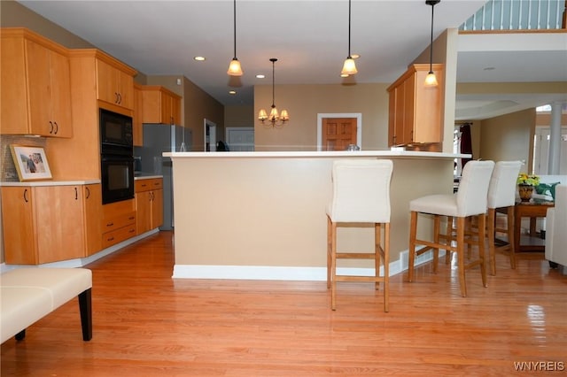 kitchen featuring light wood-style flooring, a peninsula, black appliances, a kitchen bar, and an inviting chandelier