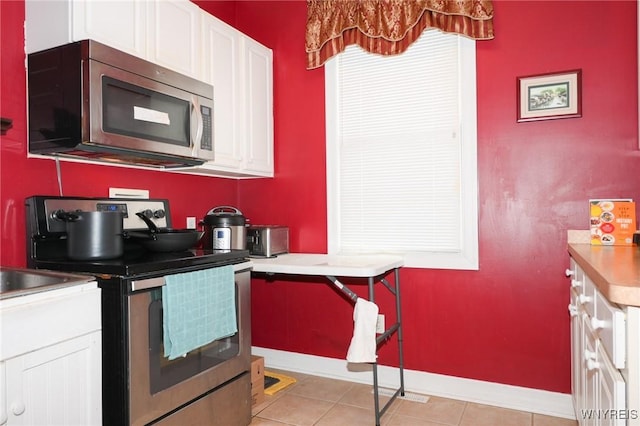 kitchen with light tile patterned floors, light countertops, appliances with stainless steel finishes, white cabinets, and baseboards