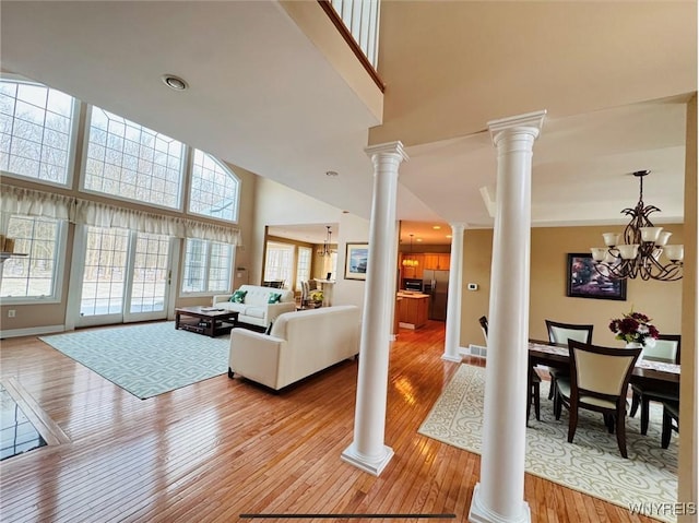 living area with light wood-style floors, an inviting chandelier, a high ceiling, and ornate columns