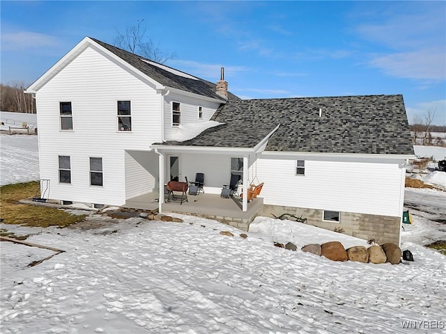 snow covered property featuring a shingled roof and a chimney