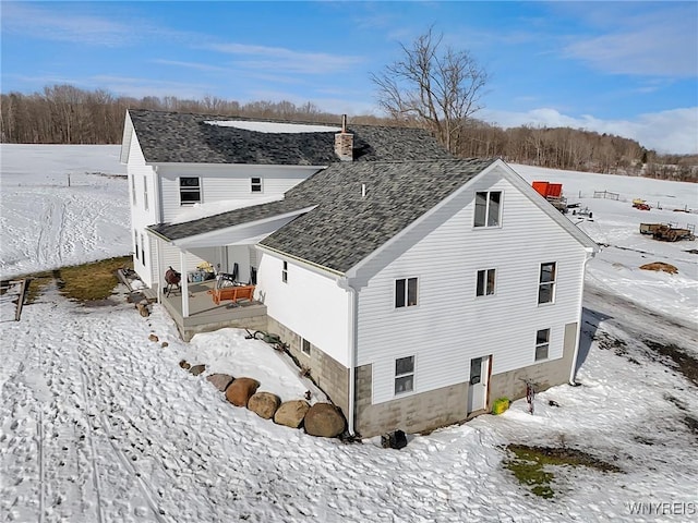 snow covered property featuring a shingled roof and a chimney