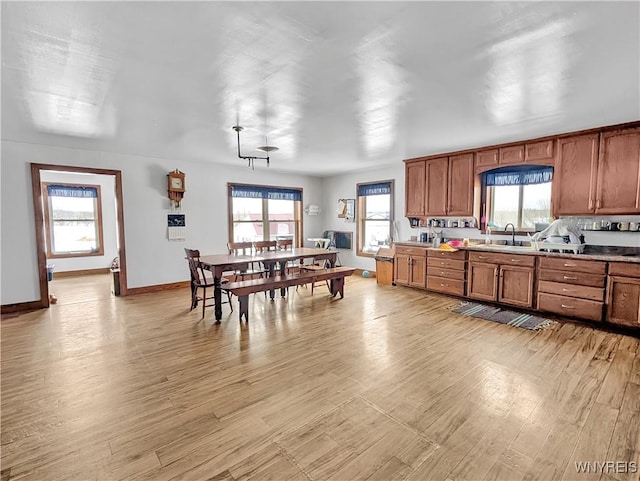 kitchen with brown cabinetry, a sink, light wood-style flooring, and baseboards