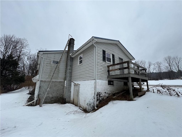 view of snowy exterior featuring a garage, a chimney, and a wooden deck