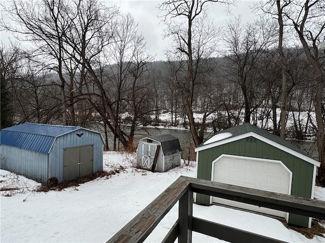 yard layered in snow featuring a garage, a shed, and an outdoor structure