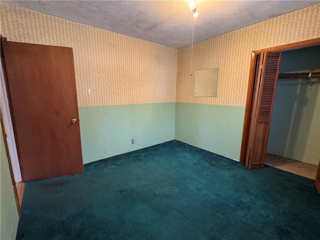 unfurnished bedroom with wallpapered walls, a textured ceiling, dark colored carpet, and a closet