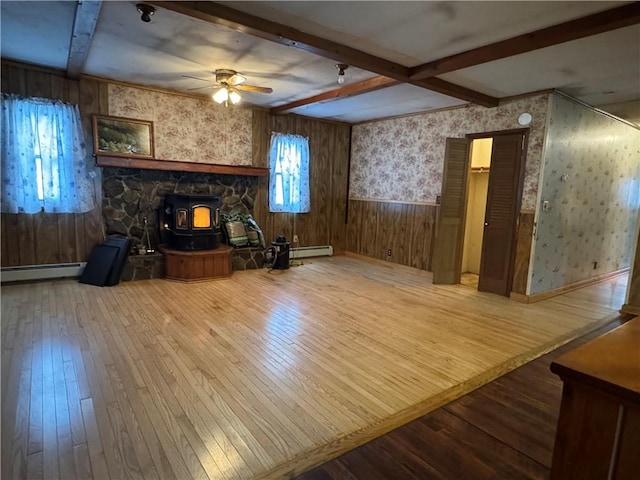 living room featuring hardwood / wood-style flooring, a wainscoted wall, baseboard heating, beam ceiling, and wallpapered walls