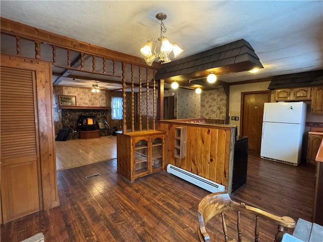 kitchen with a stone fireplace, baseboard heating, dark wood-style flooring, and freestanding refrigerator