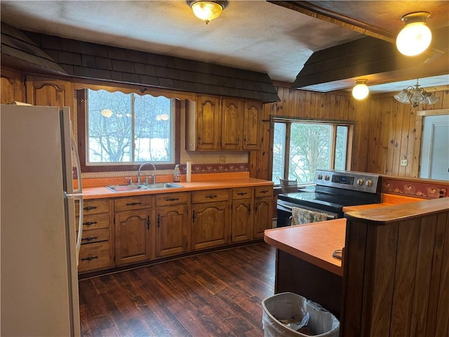 kitchen with stainless steel electric stove, brown cabinetry, a sink, and freestanding refrigerator