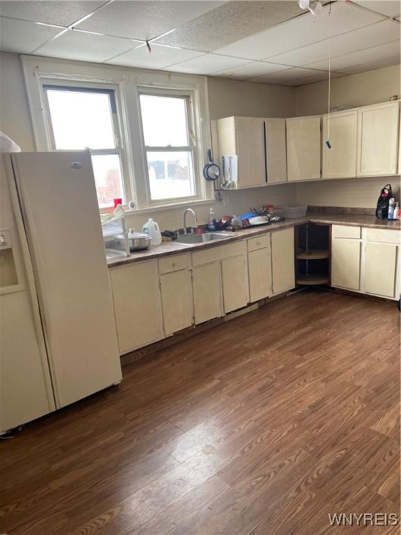 kitchen with dark wood-style floors, white refrigerator with ice dispenser, a drop ceiling, and a sink