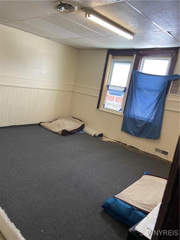 unfurnished bedroom featuring carpet floors, a drop ceiling, and wainscoting