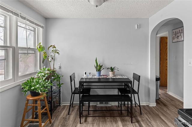 dining room with a textured ceiling, arched walkways, and wood finished floors