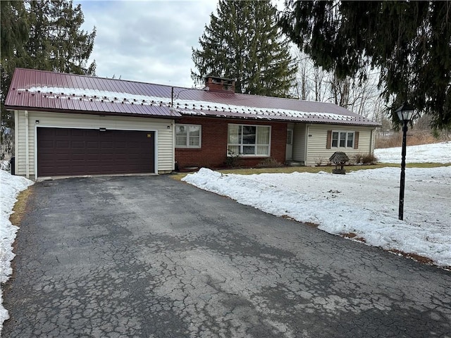 ranch-style house with a chimney, metal roof, aphalt driveway, an attached garage, and brick siding